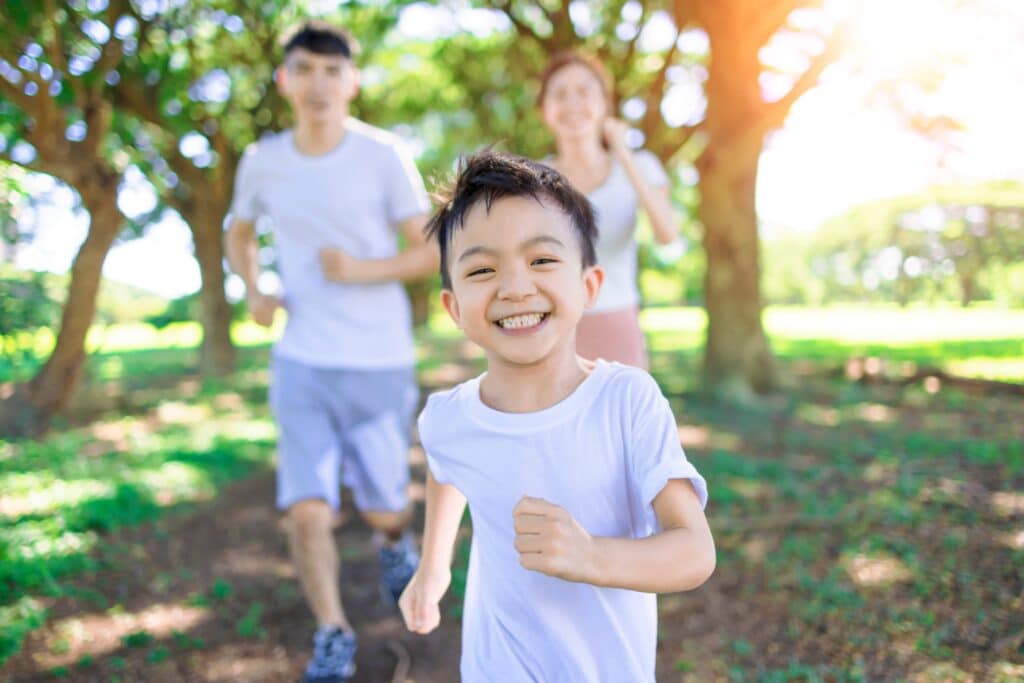 Happy Boy Jogging With Parents In The City Park