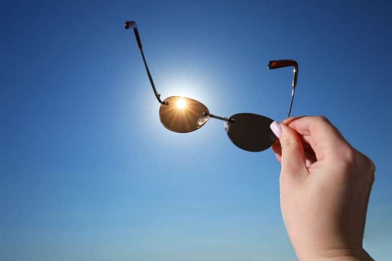 Hand holding sunglasses up in front of the sun